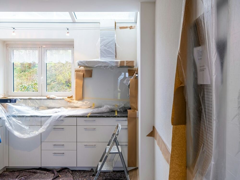 Cozinha em remodelação com móveis brancos protegidos por plástico.